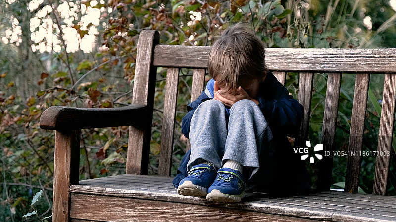 坐在长凳上捂着脸哭泣的男孩图片素材