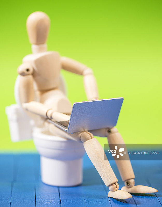 坐在马桶上使用笔记本电脑的木制人体模型图片素材