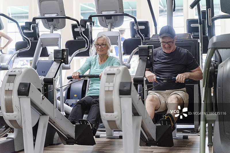 两位老人，男人和女人在健身房一起用划船模拟器做健身锻炼图片素材