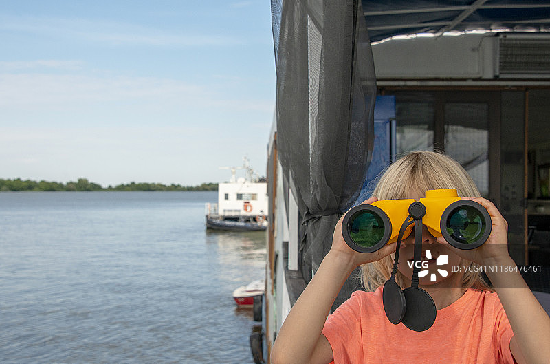 男孩手持大型双筒望远镜眺望远方，多瑙河三角洲，罗马尼亚，欧洲图片素材