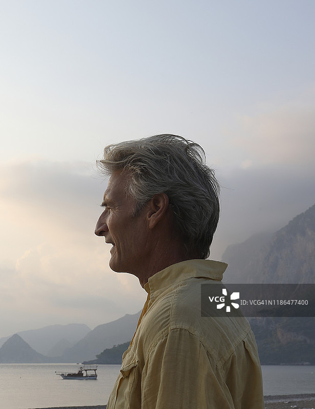 日出时分，在海滩上远眺群山的成熟男人侧面照图片素材