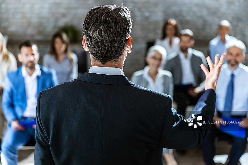 一位演讲者在会议室向一群企业家发表演讲的背影图片素材