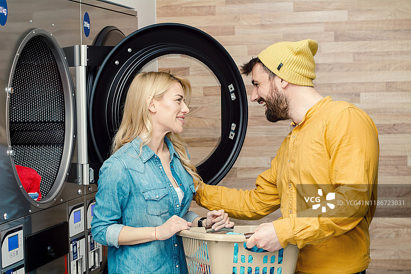 年轻快乐的夫妇在自助洗衣店一起洗衣服。图片素材