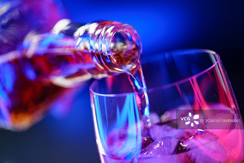 将威士忌从瓶子倒入装有冰块的玻璃杯中图片素材