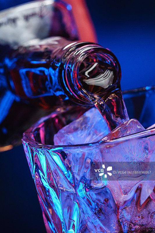 将威士忌从瓶子倒入装有冰块的玻璃杯中图片素材