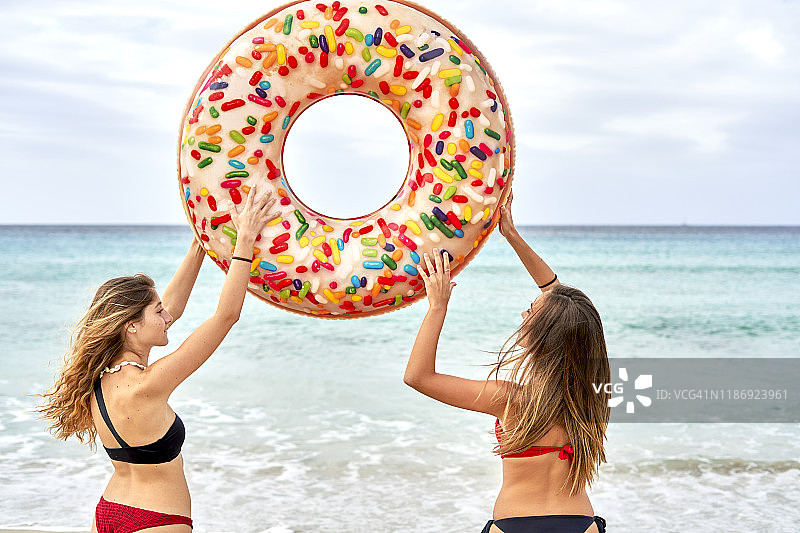 两名年轻女子站在海边，举着一个大型充气圈图片素材