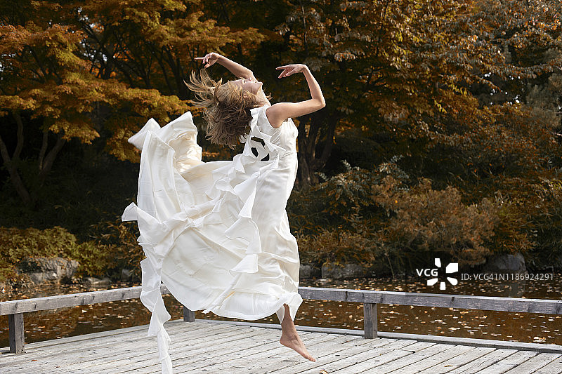 芭蕾舞演员身穿白色连衣裙在木制码头上跳跃图片素材