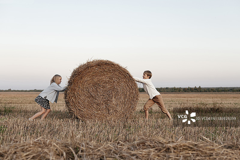 两个孩子在田野上滚动干草堆图片素材