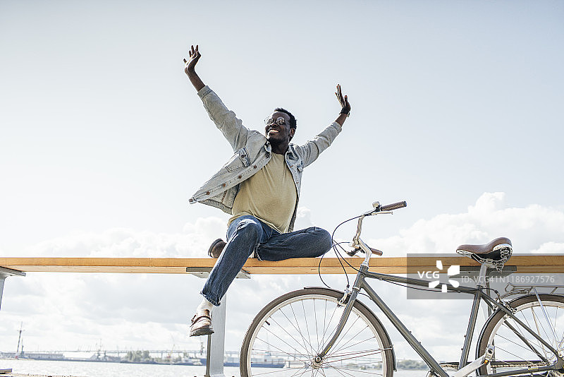 骑自行车的年轻男人坐在海边的栏杆上，假装飞翔图片素材