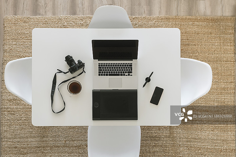 带有相机、笔记本电脑、智能手机、咖啡杯和绘图板的白色桌子，顶视图图片素材