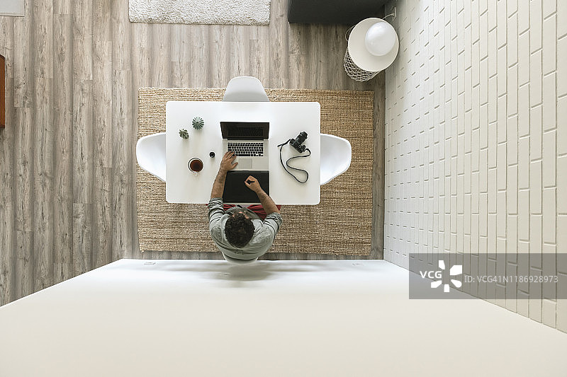 男子坐在桌旁，在绘图板和笔记本电脑上工作（顶视图）图片素材