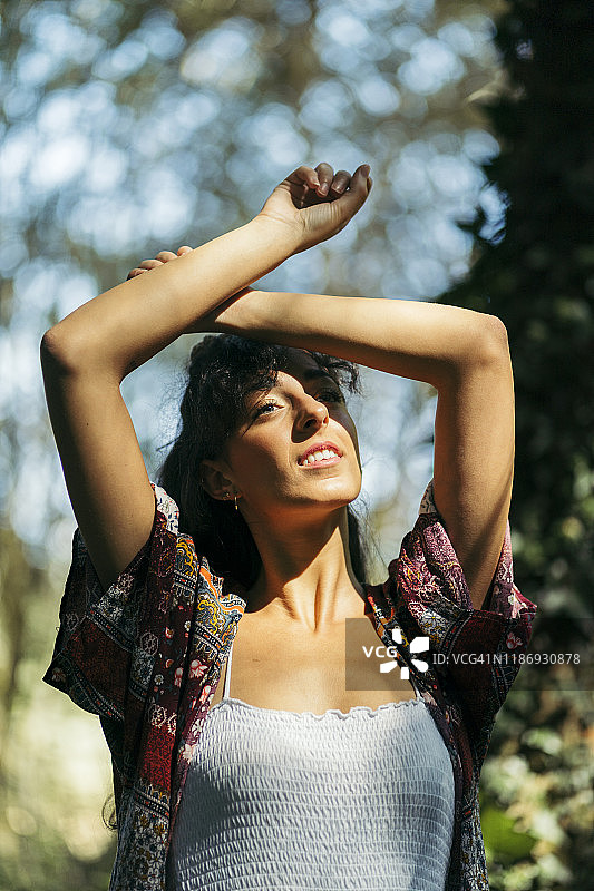 年轻女人穿着色彩鲜艳的衬衫，双手交叉在额头上，望向太阳图片素材