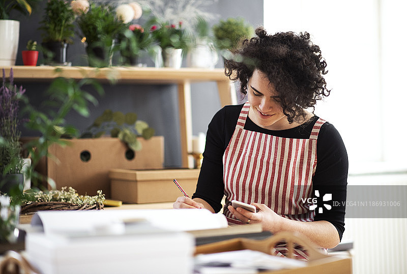 在有植物的小商店里使用手机的年轻微笑女人图片素材