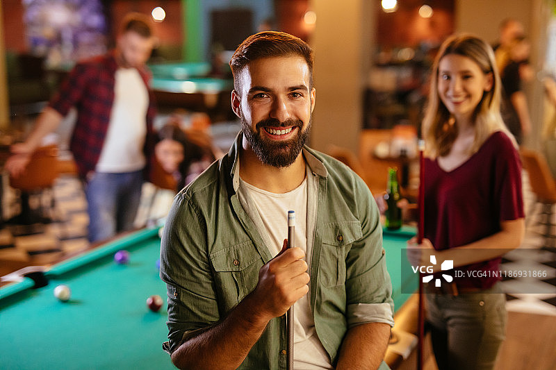 背景是朋友打台球的年轻男子肖像图片素材