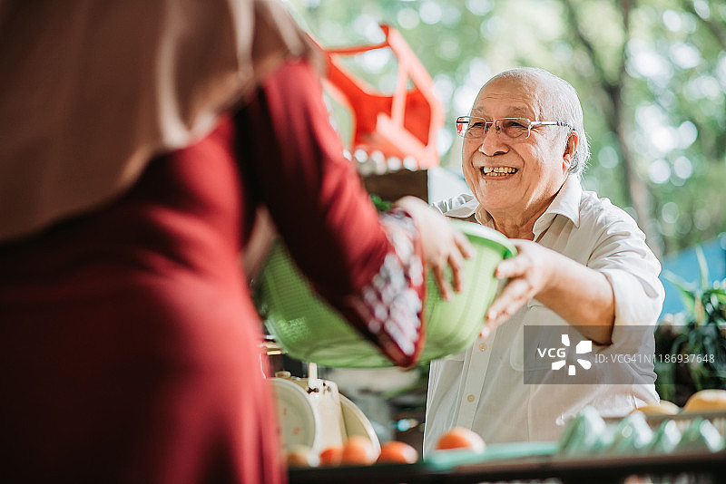 亚洲马来西亚老年男人菜摊主正在接收顾客的蔬菜篮子以计算价格图片素材