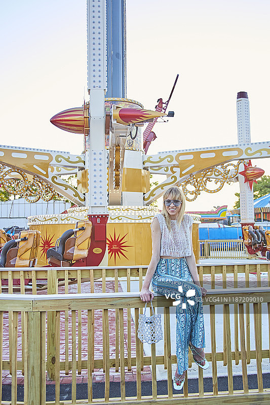 时尚金发女子坐在黄昏的嘉年华游乐设施前图片素材