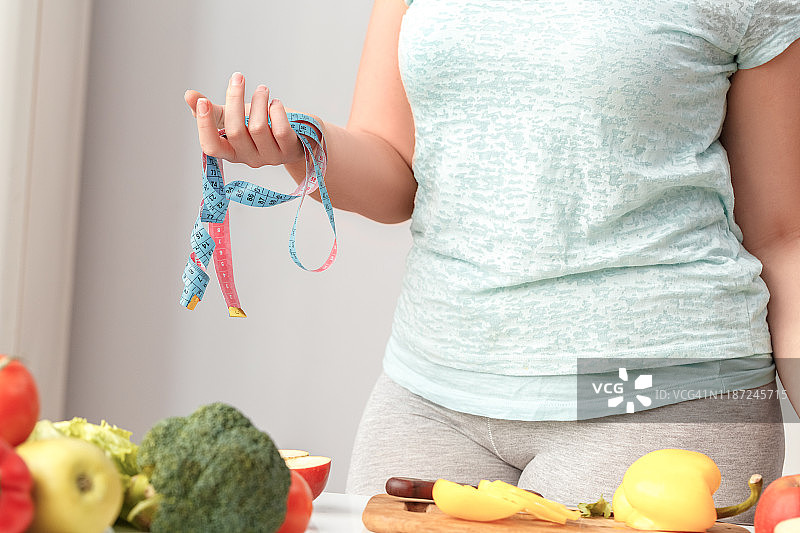 烹饪美食：站在厨房里用卷尺的胖女孩特写图片素材
