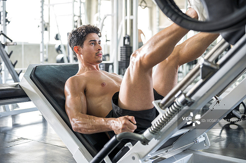 健康生活方式、锻炼与人物概念。健壮的男人在健身房的腿举机上做腿部推举图片素材