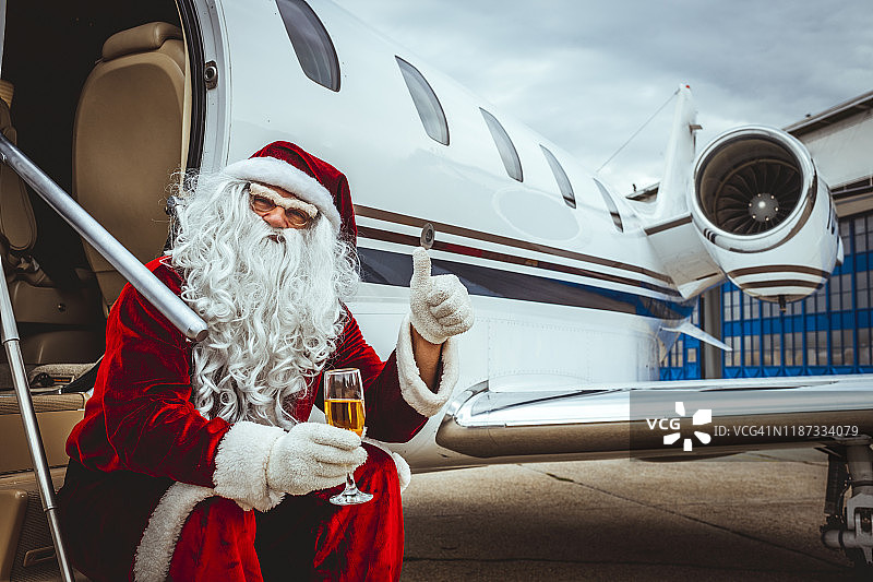圣诞老人坐在私人飞机外，手持香槟并竖起大拇指图片素材