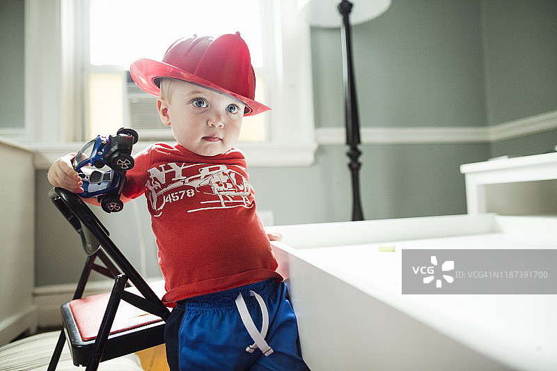 打扮成消防员的幼儿男孩拿着玩具车站起来图片素材