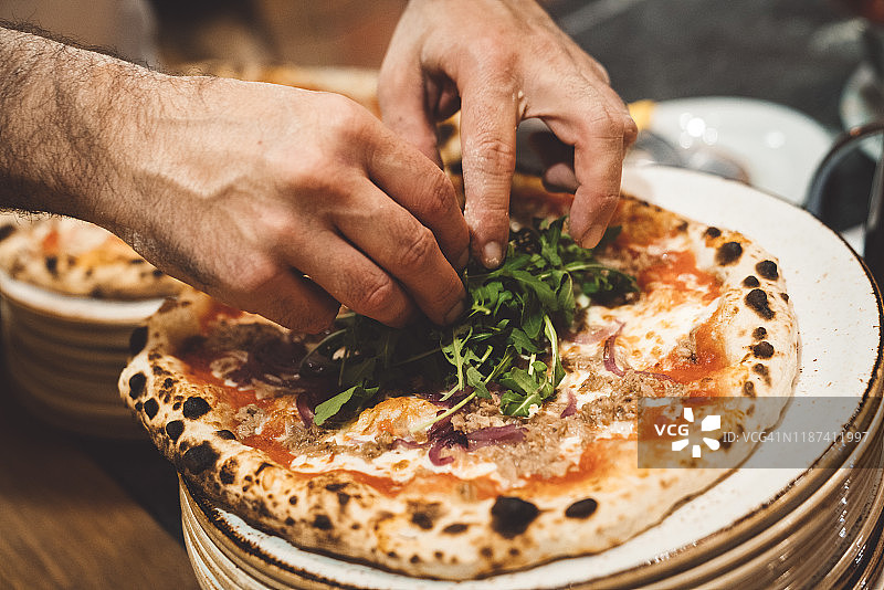 男人用手在那不勒斯披萨上放新鲜芝麻菜图片素材