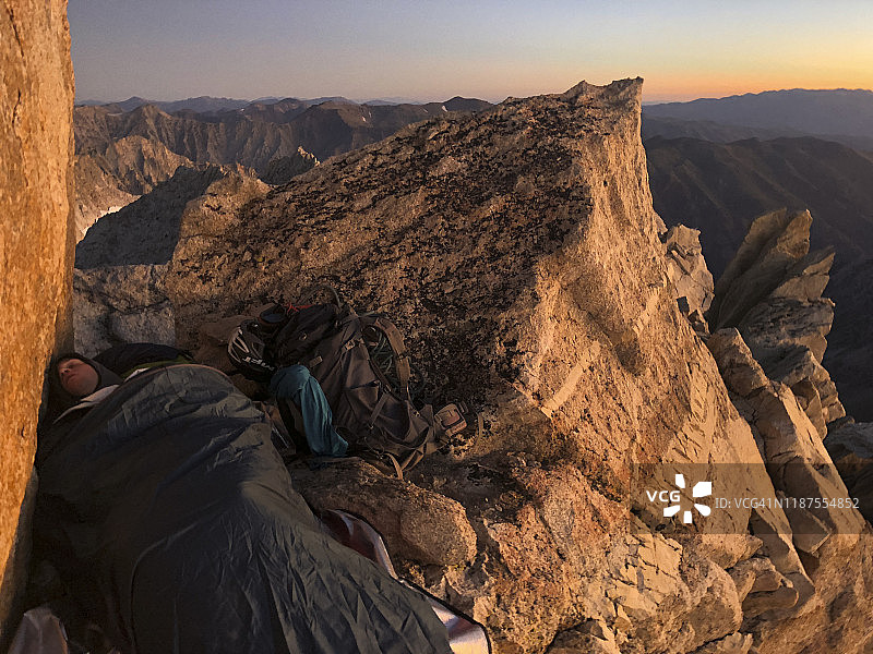 日出时分，男人睡在马特宏峰悬崖顶部的睡袋里，俯瞰锯齿岭图片素材