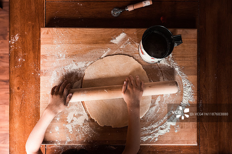 小手在桌子的木制砧板上擀面团图片素材