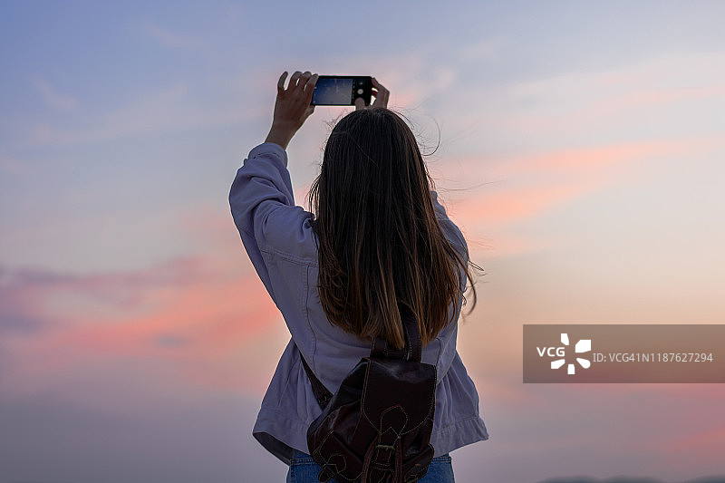 年轻女人用智能手机拍摄天空图片素材