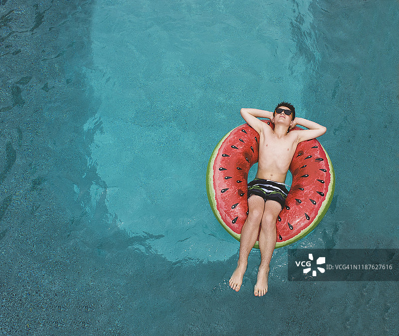 男孩在泳池中抱着西瓜充气筏的俯视图图片素材
