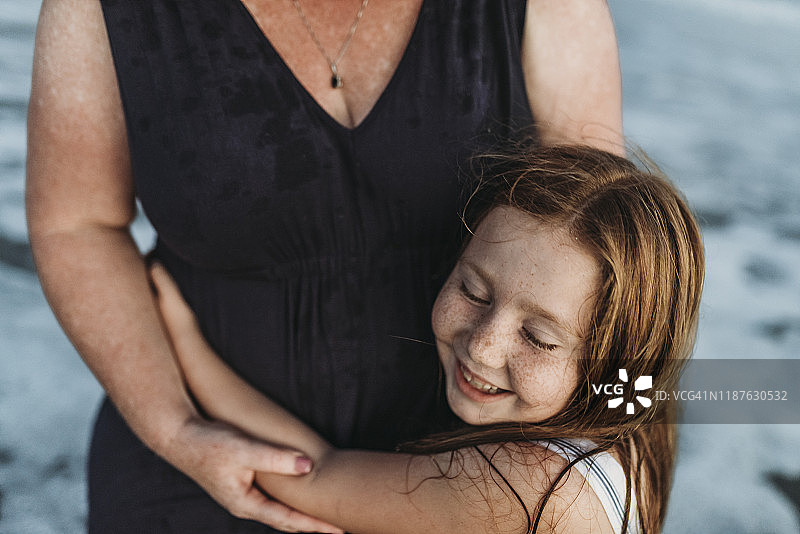 在黄昏时分，快乐的年轻女儿在海边拥抱母亲图片素材