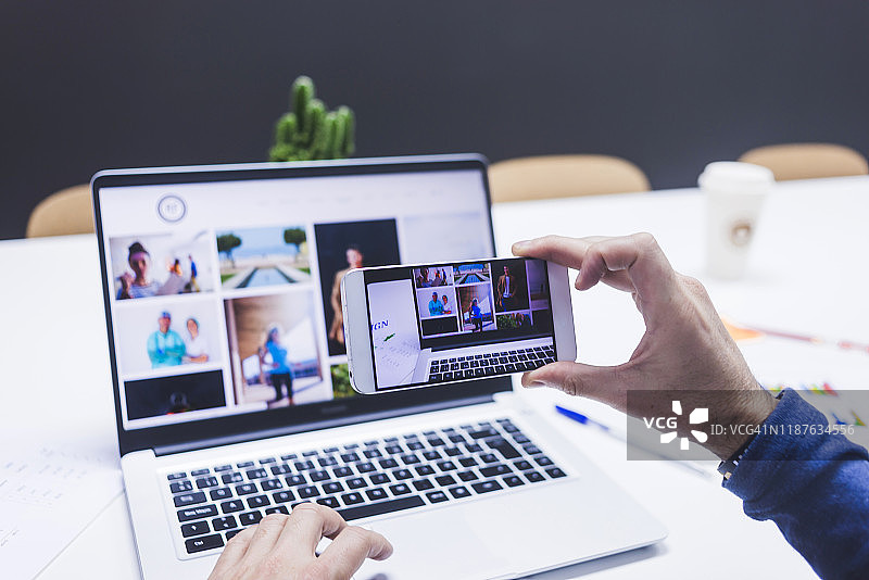 男人背影，用手机拍摄笔记本电脑图片素材