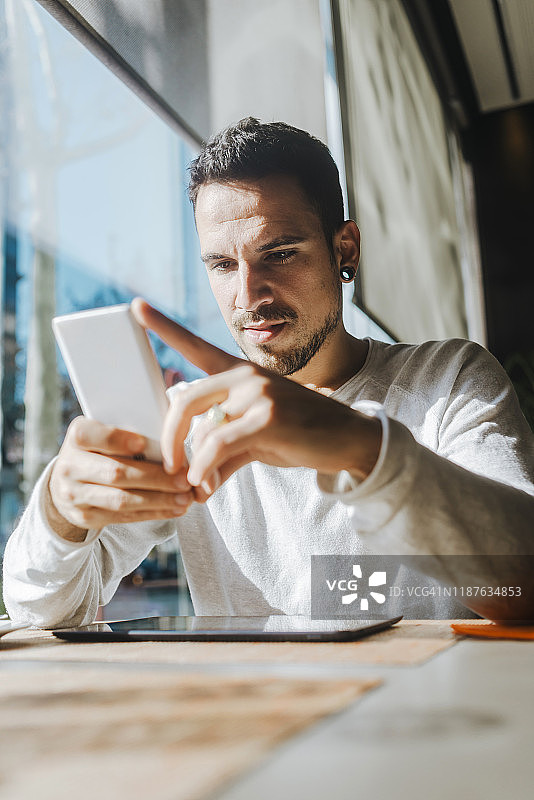 在咖啡馆工作看手机的微笑青年男子图片素材