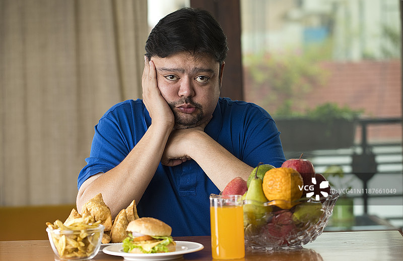 不满的男人在桌子上放着不健康和健康的食物图片素材