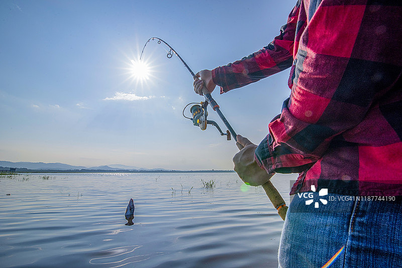 年轻人在日落时分从船上在湖上钓鱼图片素材
