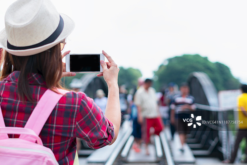 旅行中的女人在泰国北碧府桂河大桥用智能手机拍照图片素材