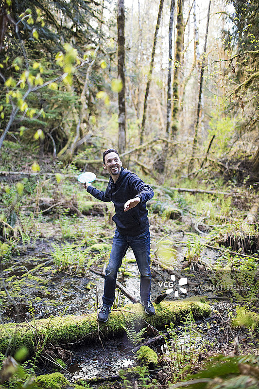 男人在森林里平衡倒下的树木时扔飞盘图片素材