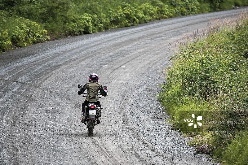 女人在加拿大骑摩托车行驶在碎石路上图片素材
