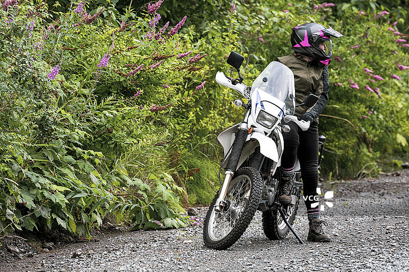 一位女士骑摩托车休息，和她的自行车站在一起图片素材