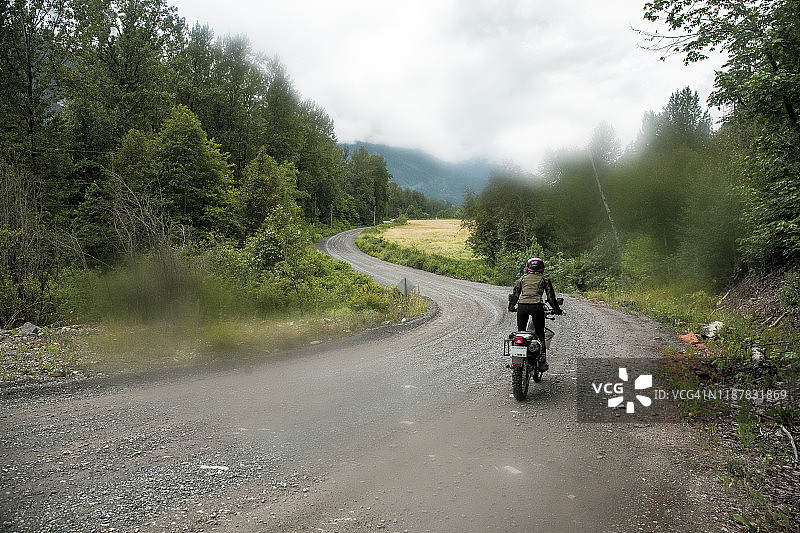女人在加拿大骑摩托车行驶在碎石路上图片素材