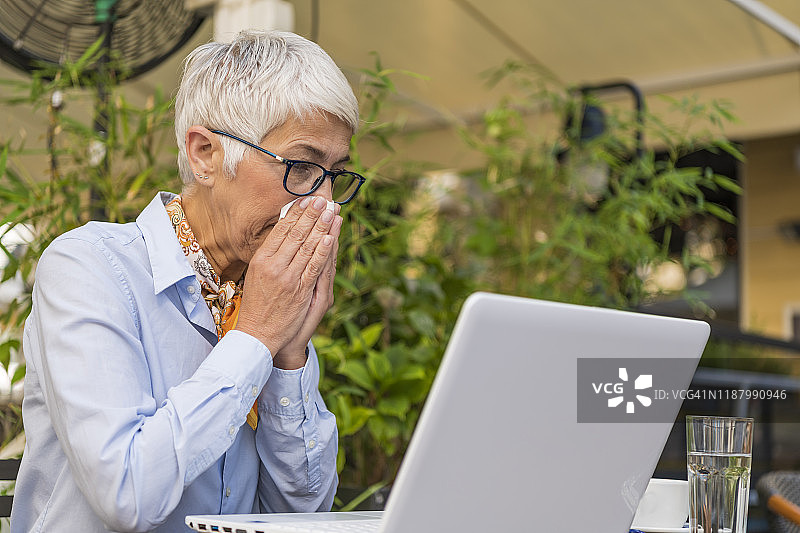 患有过敏问题的老年妇女用纸巾擦鼻子图片素材