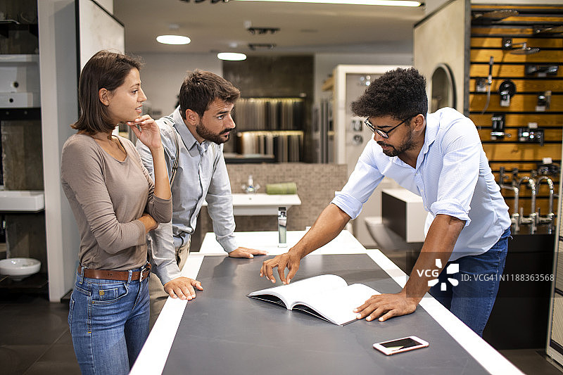 夫妻在浴室瓷砖店与店主交谈，店主靠在桌子上介绍产品图片素材