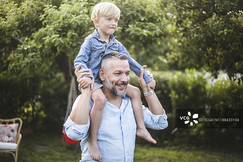 微笑的中年男人在后院肩扛儿子玩耍图片素材