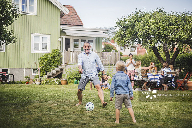父亲与儿子踢足球，朋友后院聚会图片素材