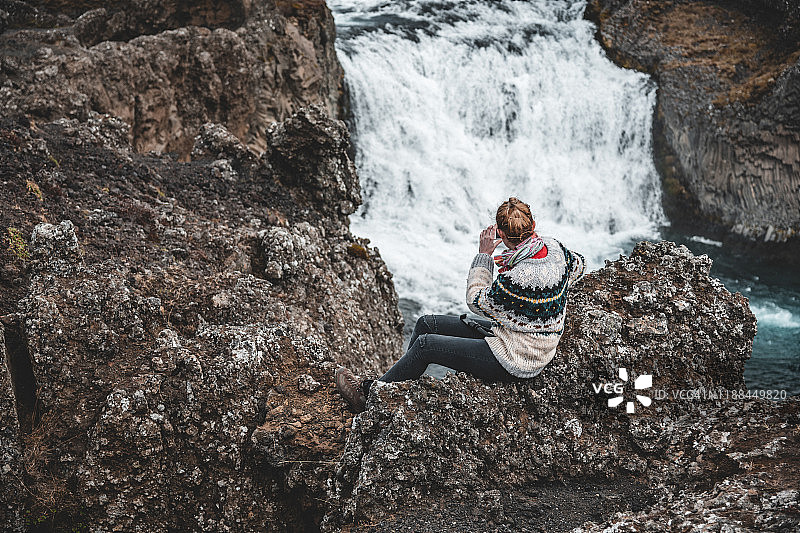 女人坐在悬崖上拍摄瀑布图片素材
