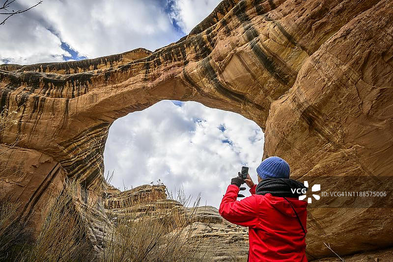 游客拍摄美国犹他州天然桥国家纪念碑锡帕普桥的岩石拱门图片素材