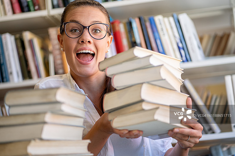 在图书馆抱着一堆书的快乐年轻女人图片素材