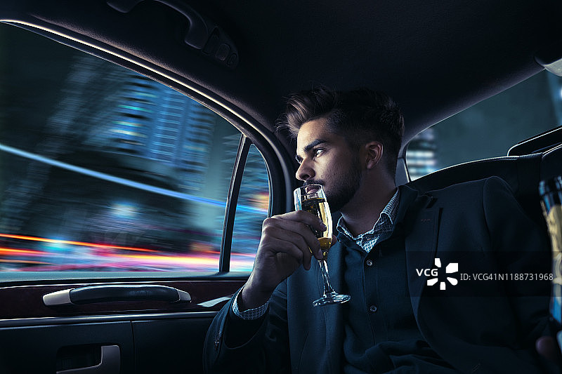 乘坐豪华轿车，在夜晚的城市里喝香槟的商人图片素材