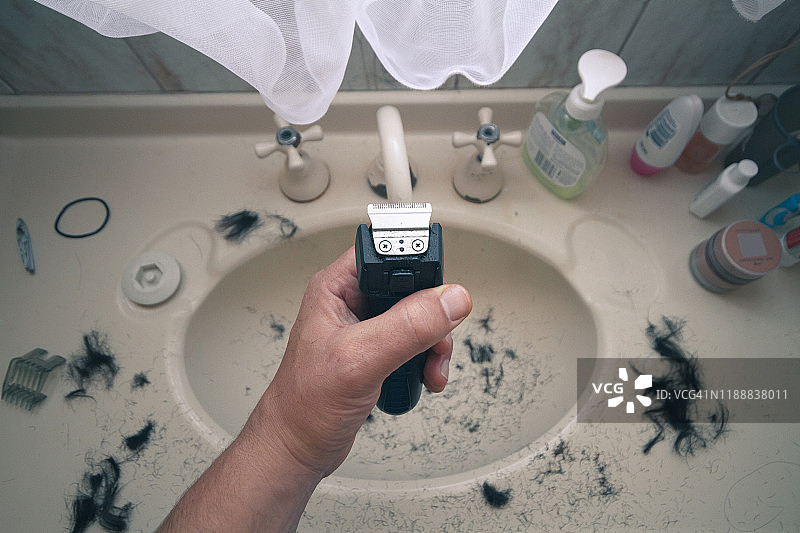 男人拿着电动剃须刀，水槽里到处都是头发图片素材