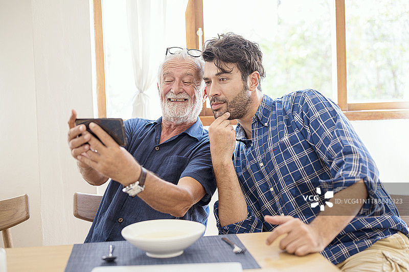 快乐的络腮胡退休父亲和开朗的儿子在家一起自拍图片素材