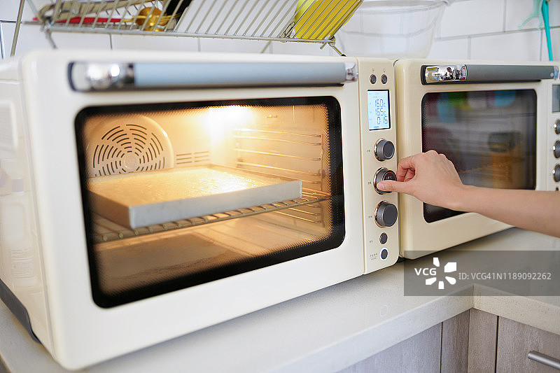 年轻的亚洲女性用烤箱做蛋糕图片素材